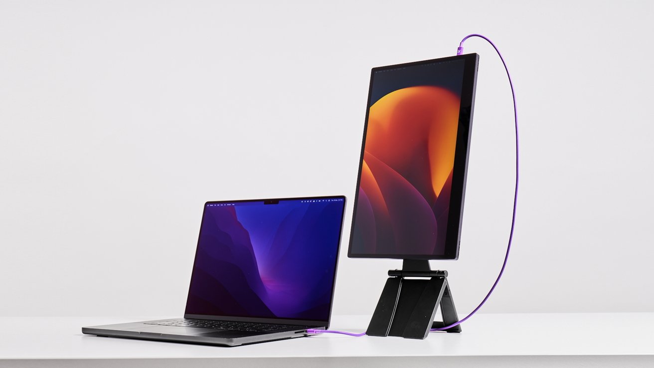 Open laptop and vertical tablet on a white desk connected by a purple cable, displaying abstract purple and orange wallpapers.