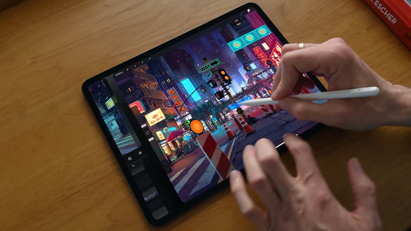 Person using a stylus to create colorful digital cityscape artwork on a tablet, placed on a wooden surface.