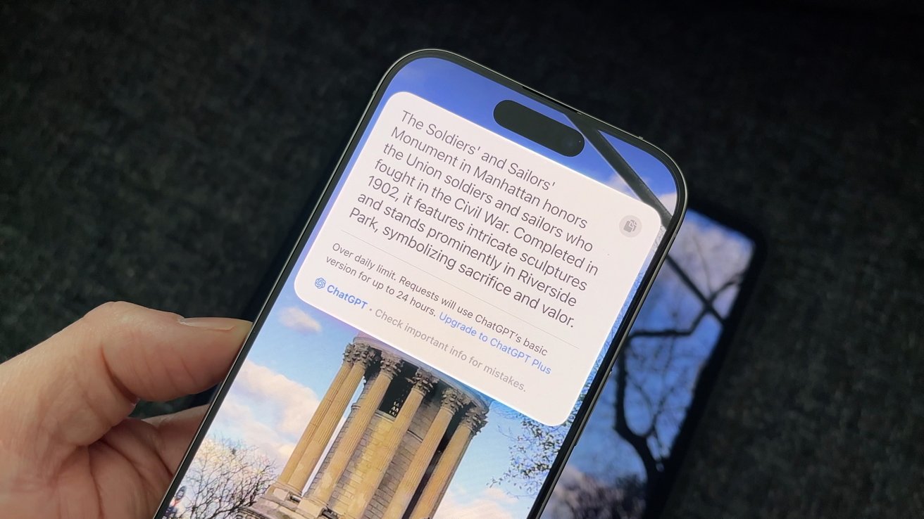 Hand holding a smartphone displaying text about the Soldiers' and Sailors' Monument, with a background image of the monument's columns and bare tree branches.