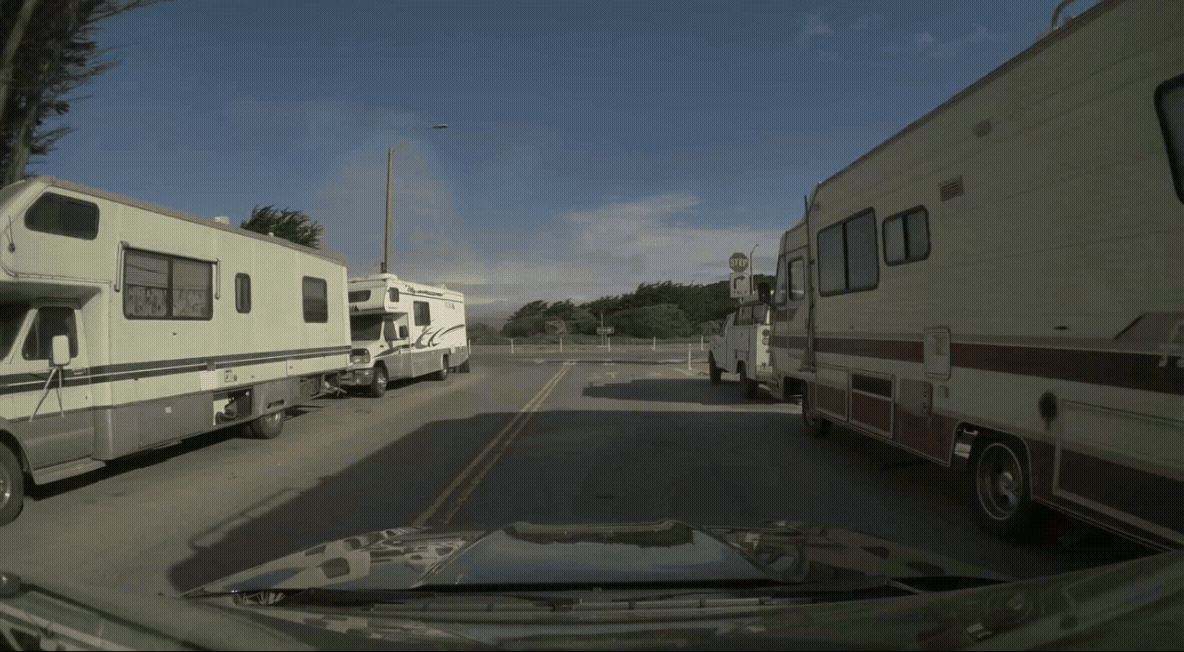 drivers-perspective-gif-1 GIF of a car driving down a street with parked vehicles and a visible Stop sign near a curve.