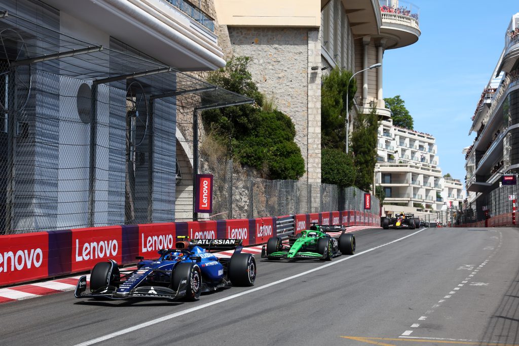 Two Formula 1 race cars driving through Monaco alongside Lenovo branded banners.